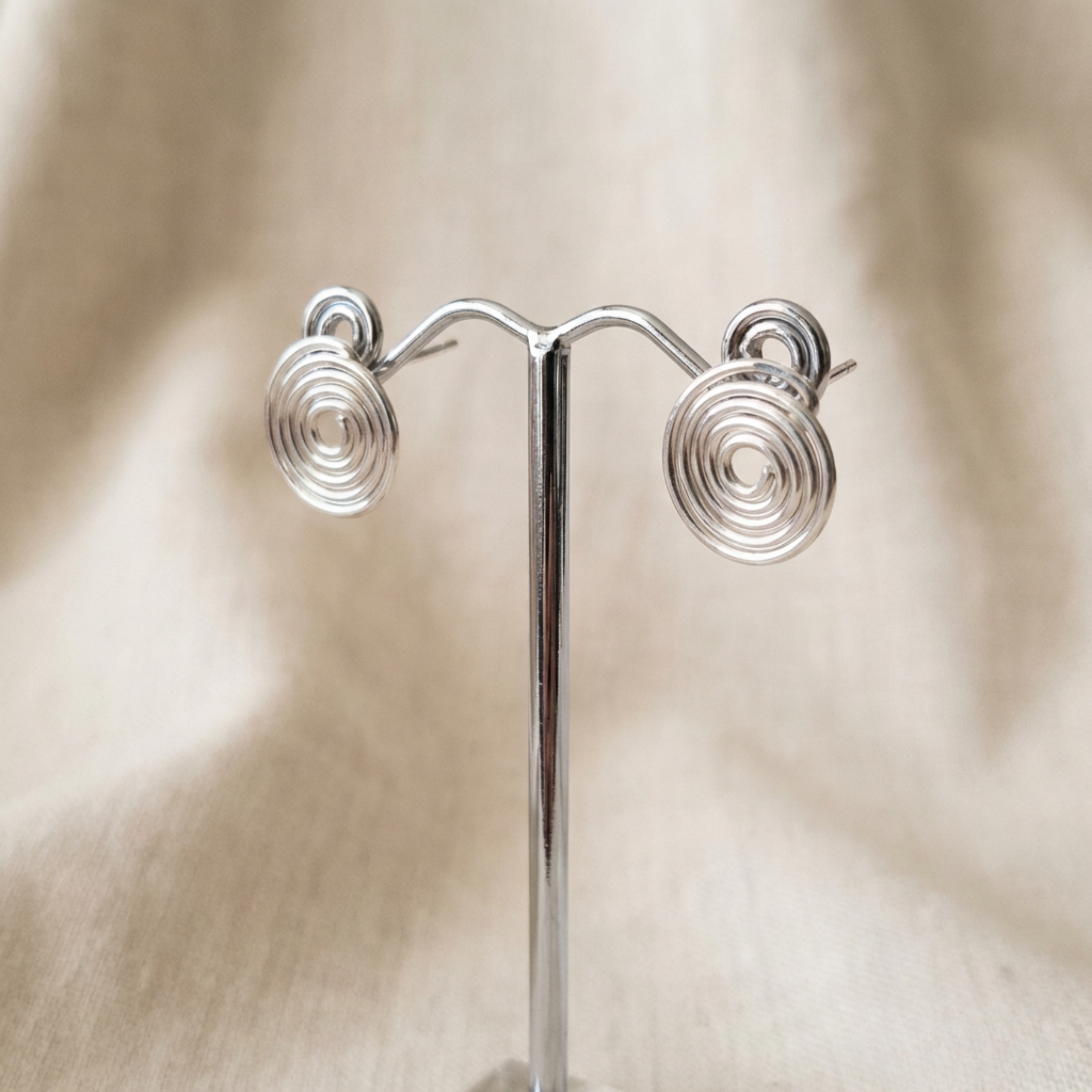Silver spiral earrings on a stand against a beige fabric background