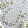 Silver necklace with circular design and half chain on a textured surface with white flowers