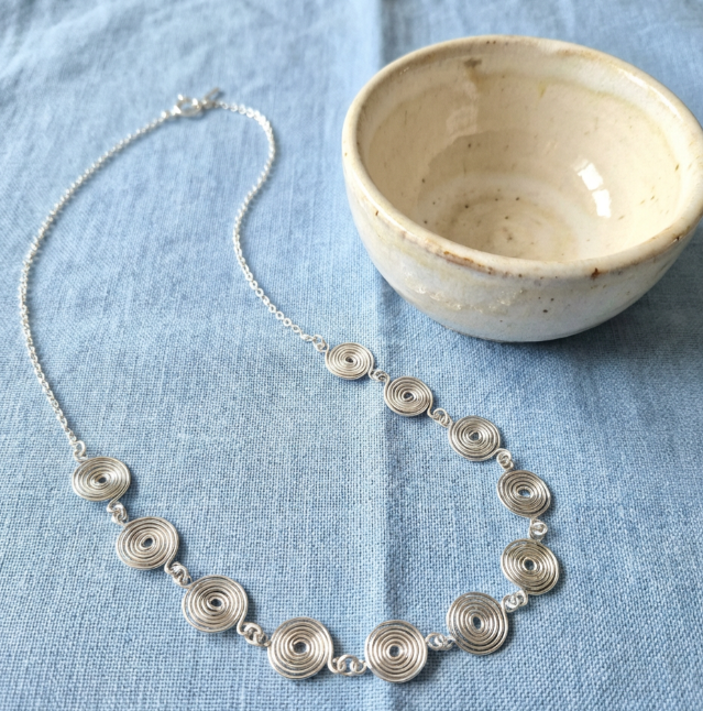 Silver necklace with circular design on a blue fabric background