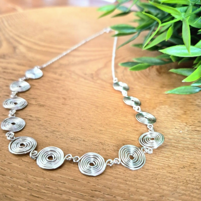 Closed Silver Spiral Necklace with chain on a wooden background