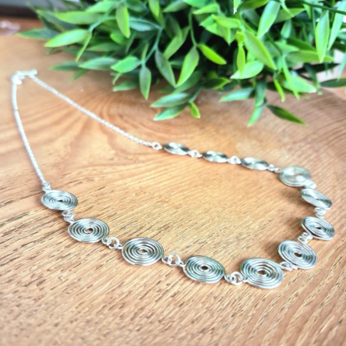 Side view of a silver spiral necklace with chain on a wooden background