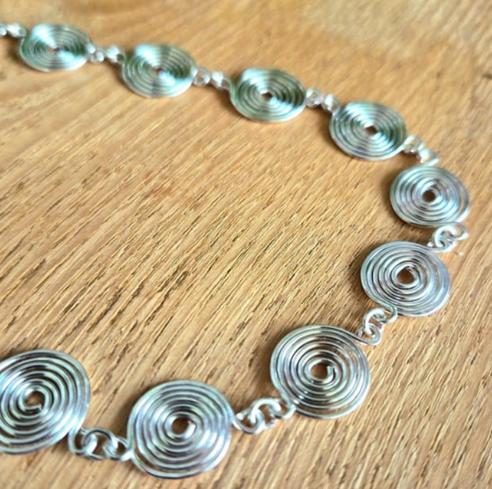 Close up view of the spirals in this silver spiral necklace on a wooden background