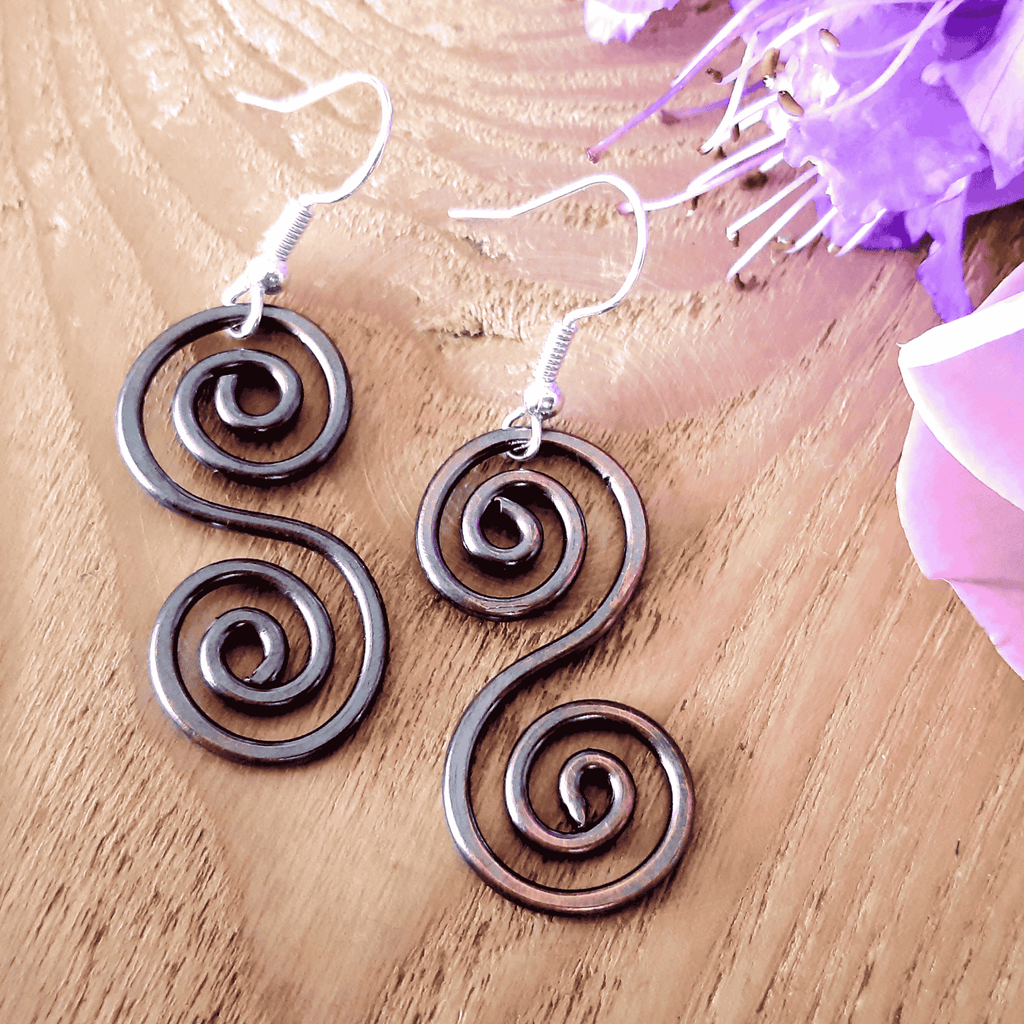 Copper Celtic earrings on a wooden surface with purple flowers
