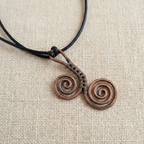 Copper spiral pendant on a black cord against a beige fabric background
