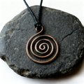 Copper spiral pendant on a black cord against a dark stone background