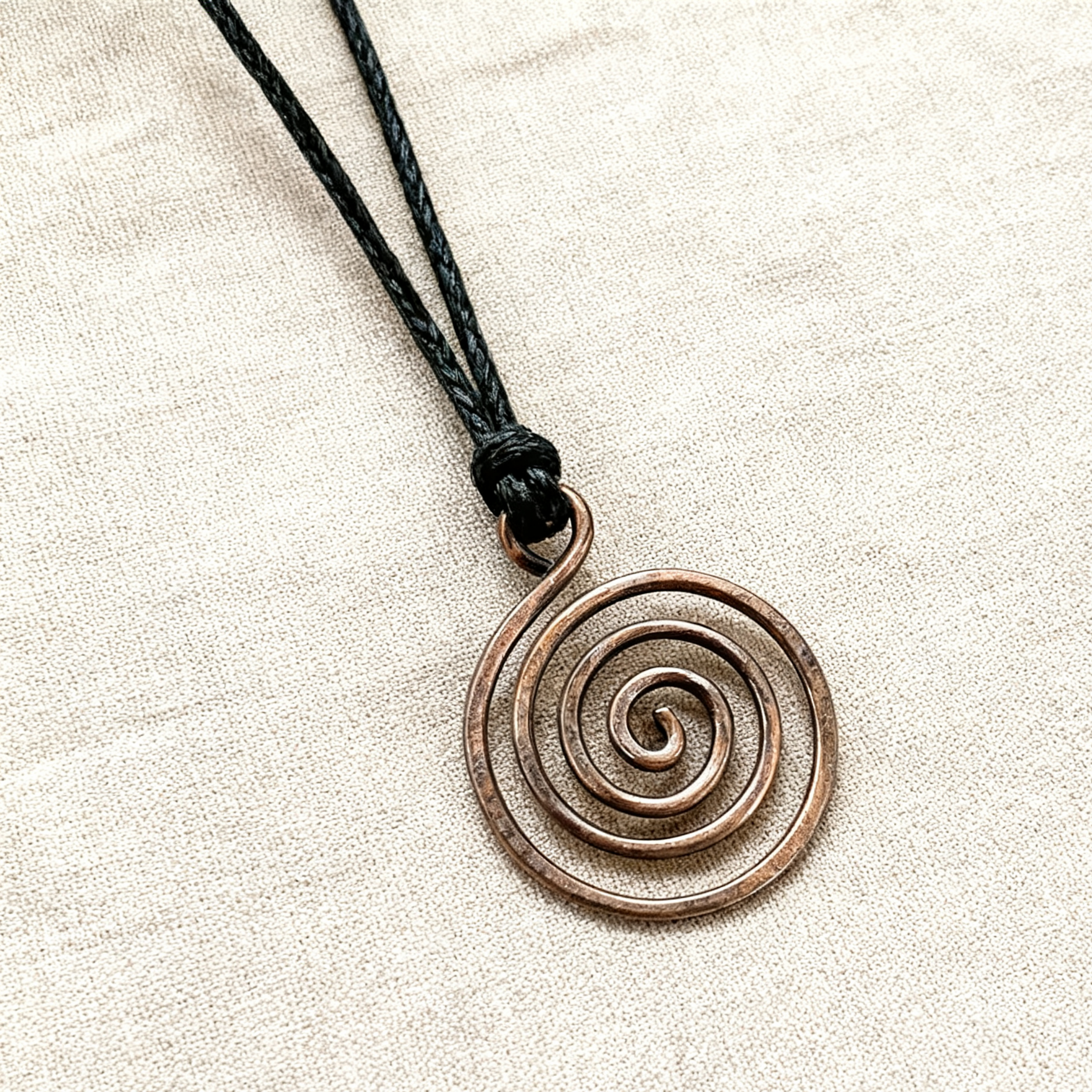 Bronzed copper spiral pendant on a black cord against a beige background