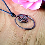 Copper spiral necklace on a wooden surface with pink flowers