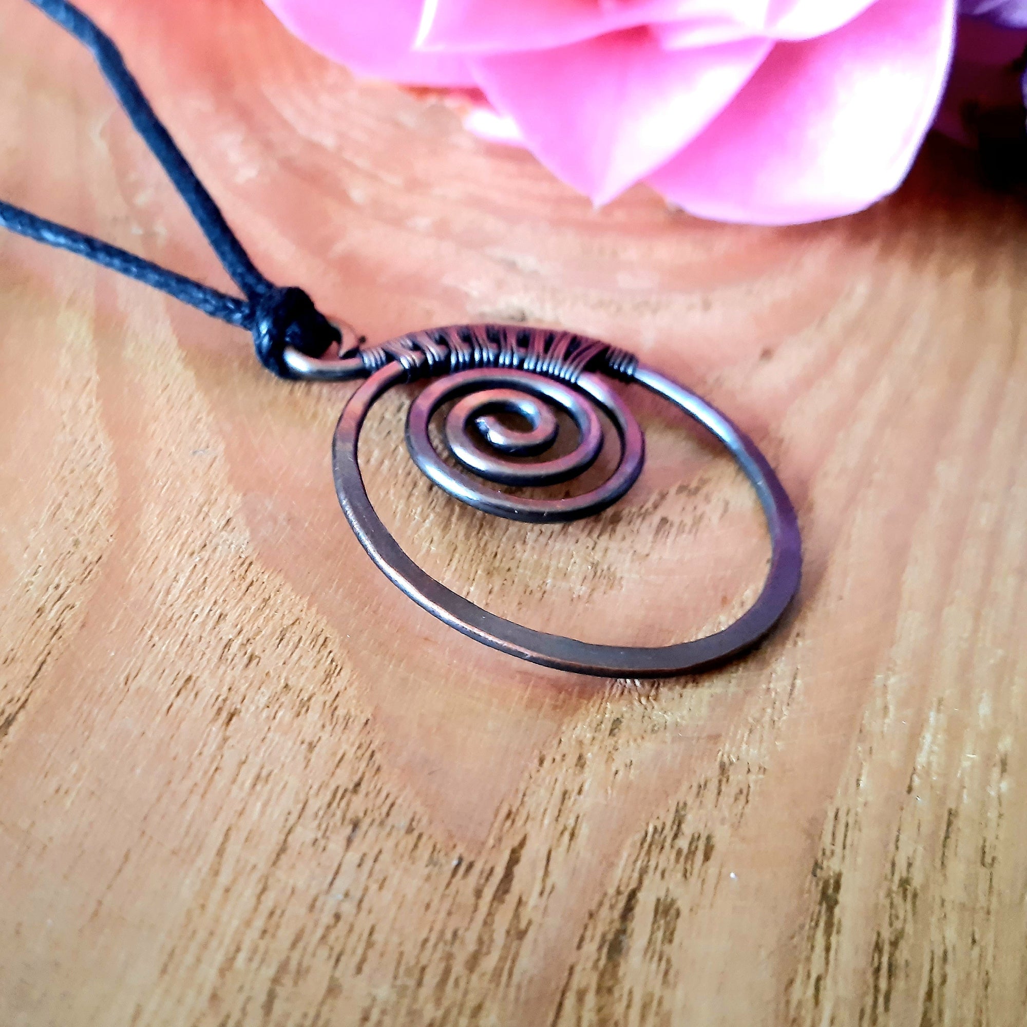 Copper spiral necklace on a wooden surface with pink flowers