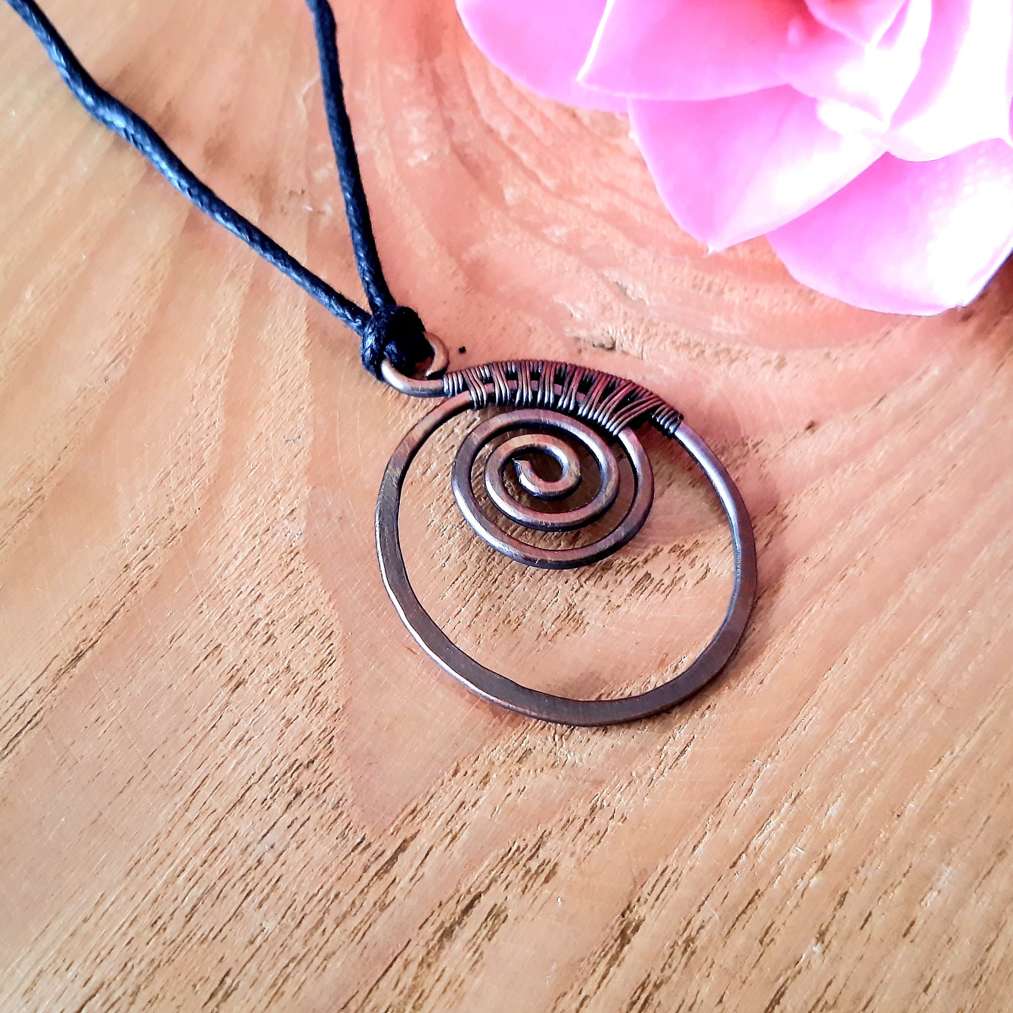 Copper spiral pendant necklace on a wooden surface with pink flowers