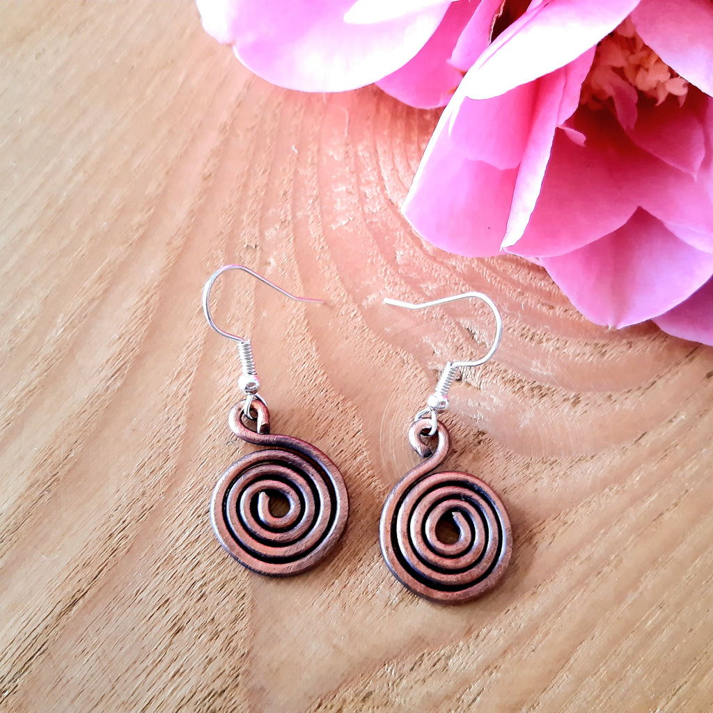 Copper spiral earrings on a wooden surface with a pink flower in the background