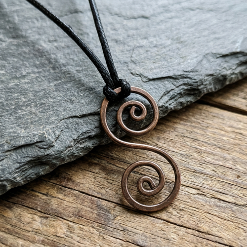 Copper spiral pendant on a black cord against a stone and wood background