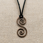 Bronze copper spiral pendant on a black cord against a beige fabric background