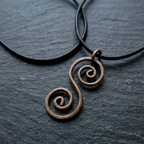 Copper spiral pendant on a black cord against a dark grey background