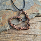 Copper wire-wrapped pendant on a black cord against a stone background