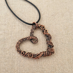 Copper heart-shaped pendant on a black cord against a beige fabric background