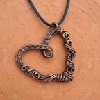 Copper heart-shaped pendant on a cord against a brown background