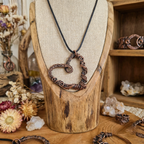 Copper heart-shaped pendant on a wooden stand with a rustic display background