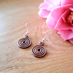 Copper spiral earrings on a wooden surface with a pink flower.
