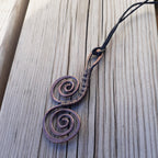 Copper spiral pendant on a black cord against a wooden background