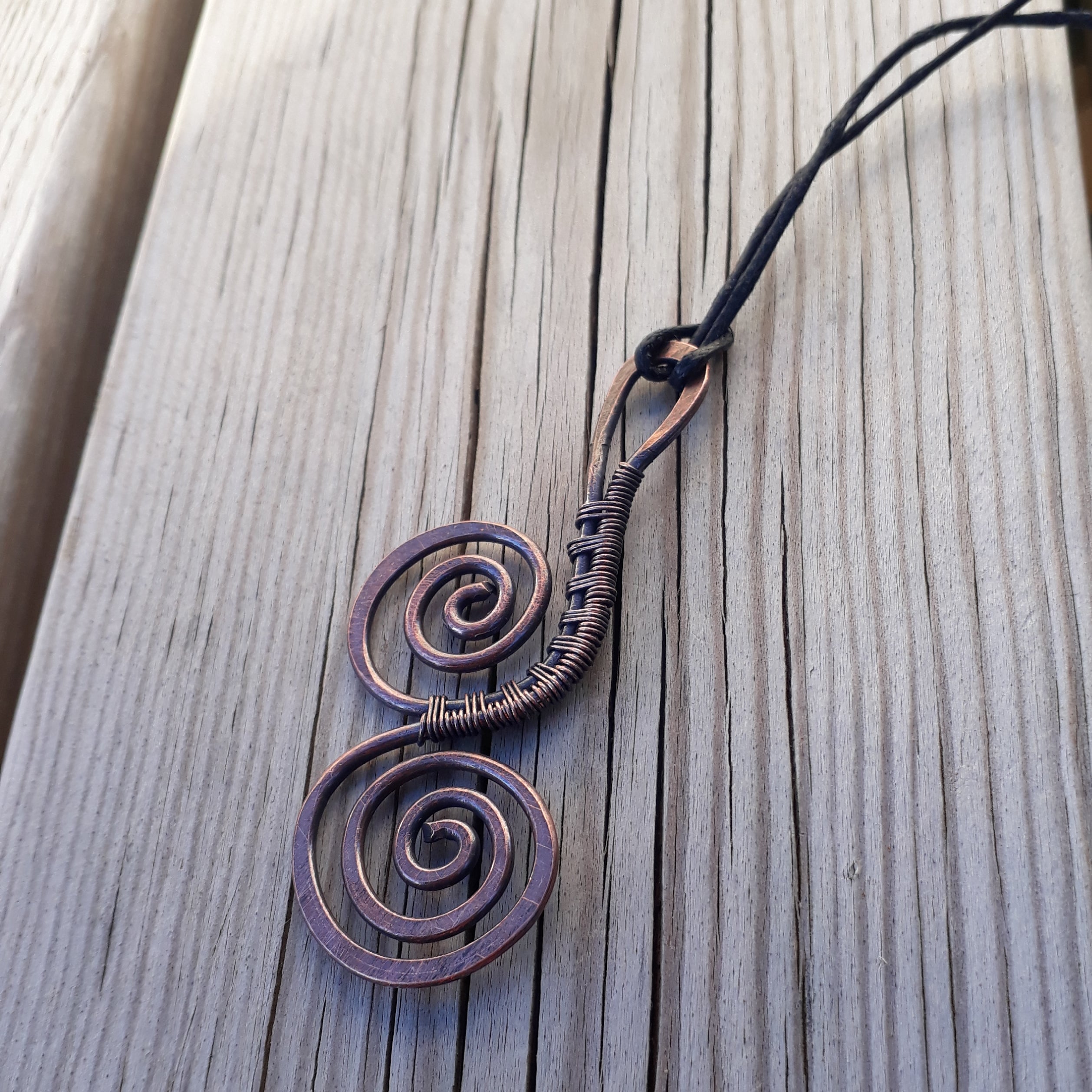 Copper spiral pendant on a black cord against a wooden background