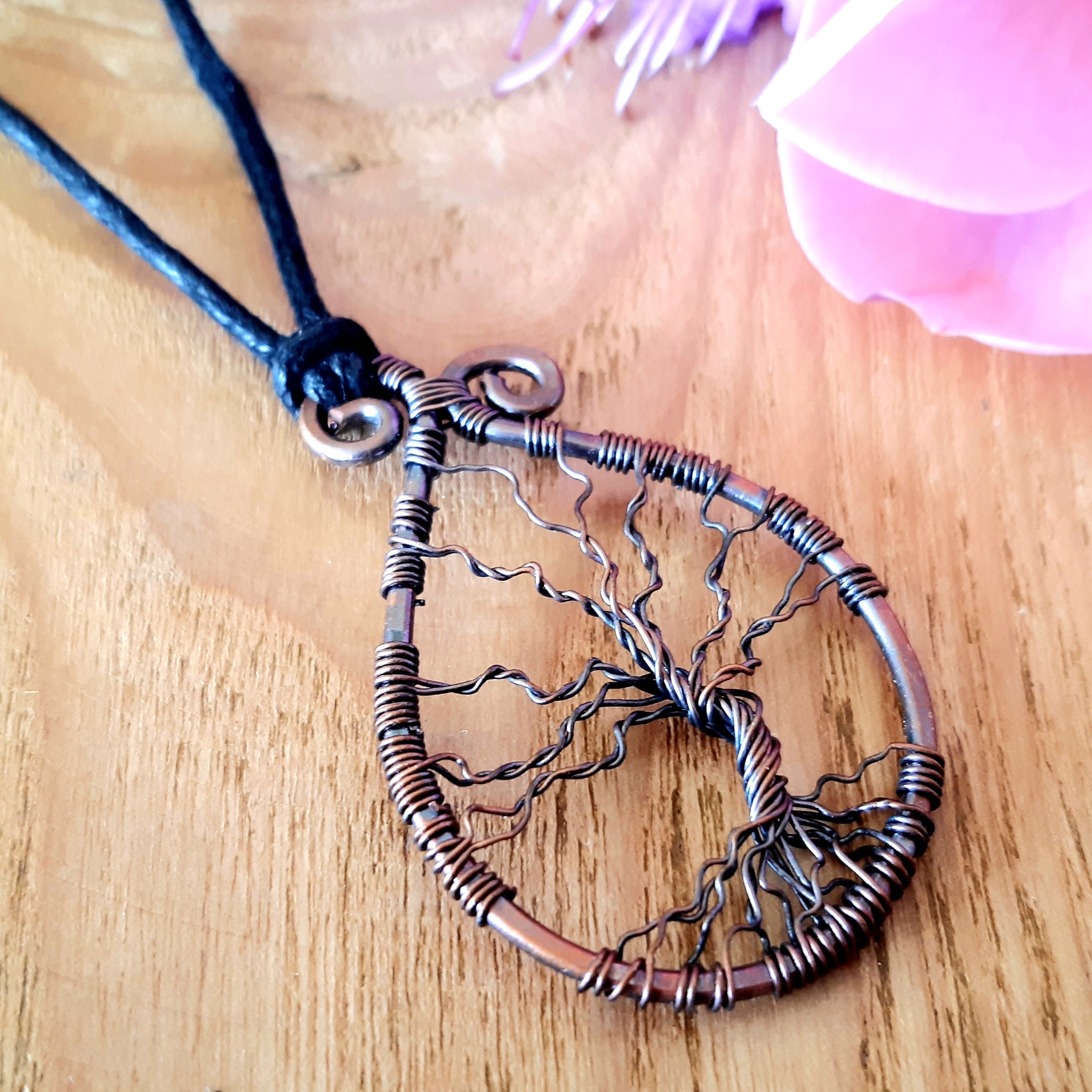 Copper tree of life necklace on a wooden surface with a pink flower in the background