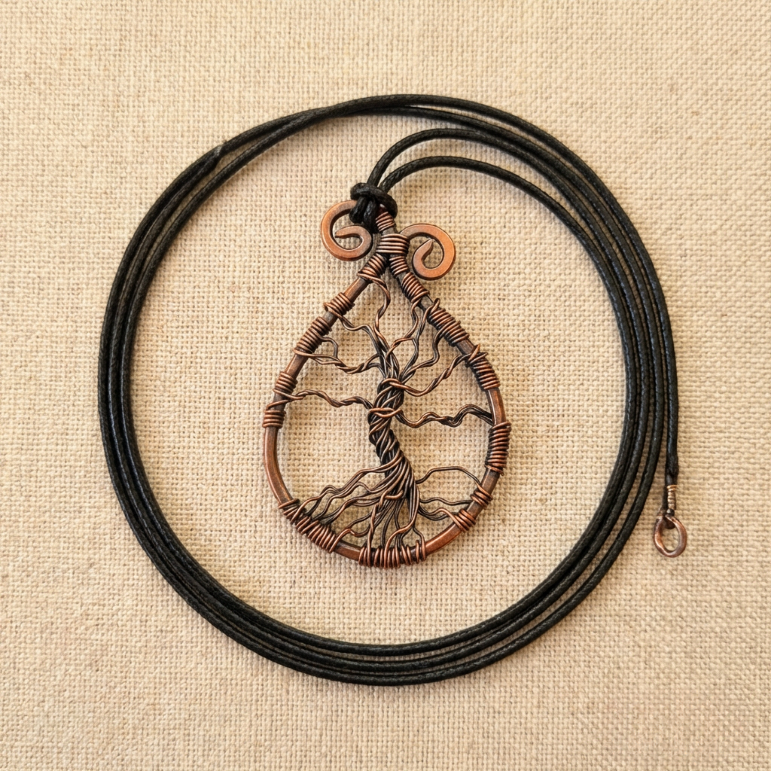 Copper tree of life pendant on a black cord against a beige fabric background