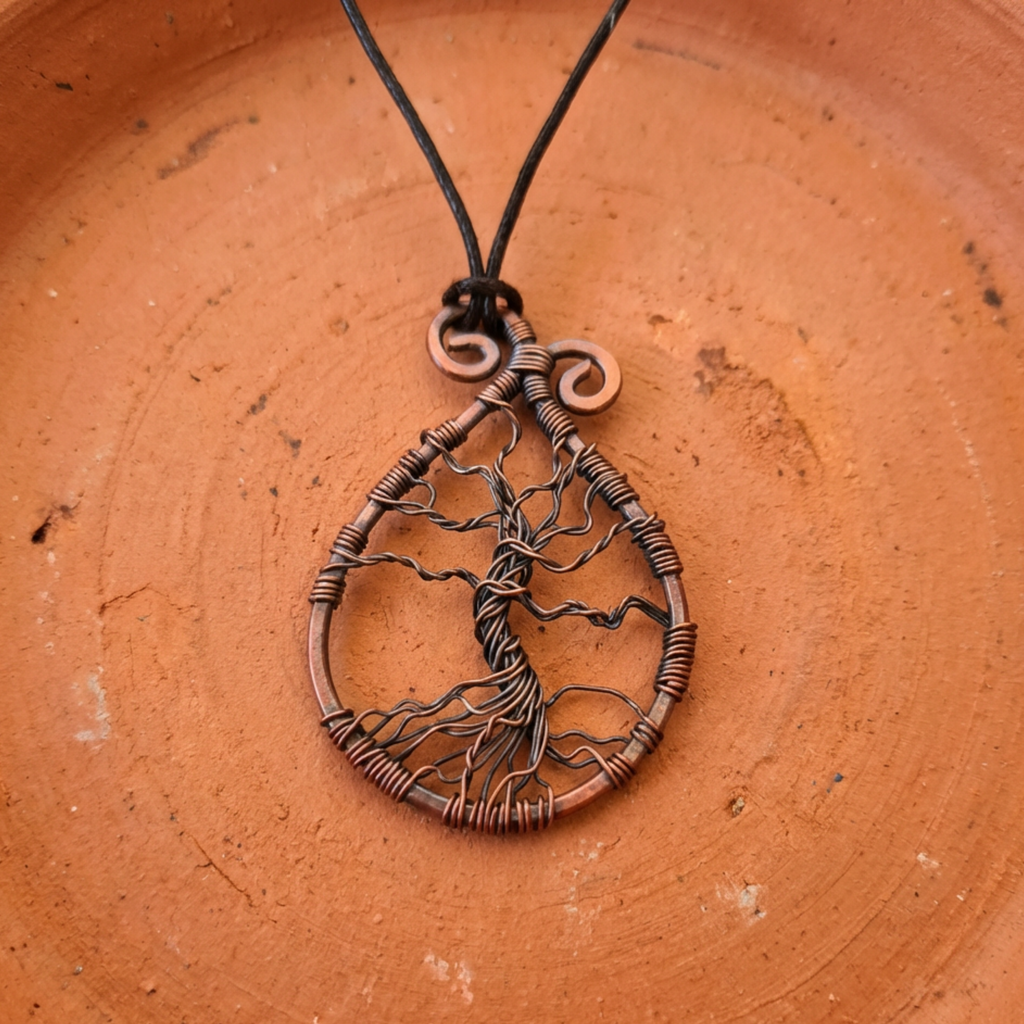 Copper tree of life pendant on a string against a terracotta background