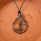 Copper tree of life pendant on a string against a terracotta background