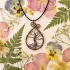 Bronze tree-shaped pendant on a black cord surrounded by pressed flowers and leaves