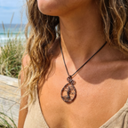 Person wearing a necklace with a tree of life pendant on a beach