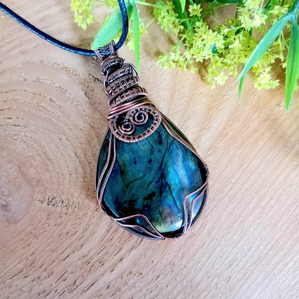 Blue pendant necklace on a wooden surface with green leaves in the background