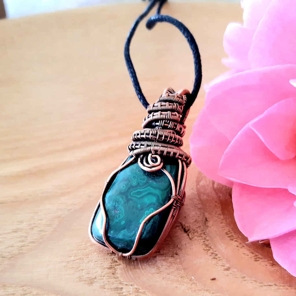 Malachite pendant on a cord with a pink flower on a wooden surface