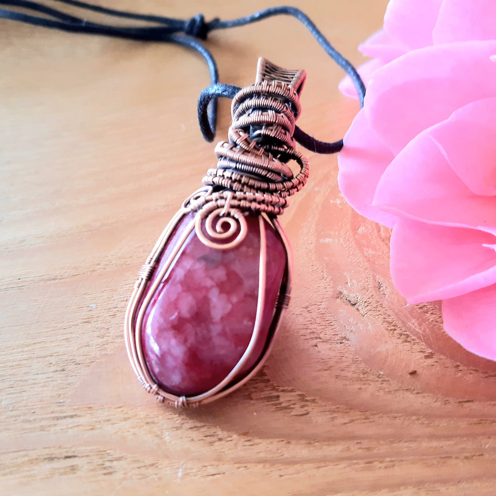 Pink pendant with silver wire wrapping on a wooden surface with a pink flower.