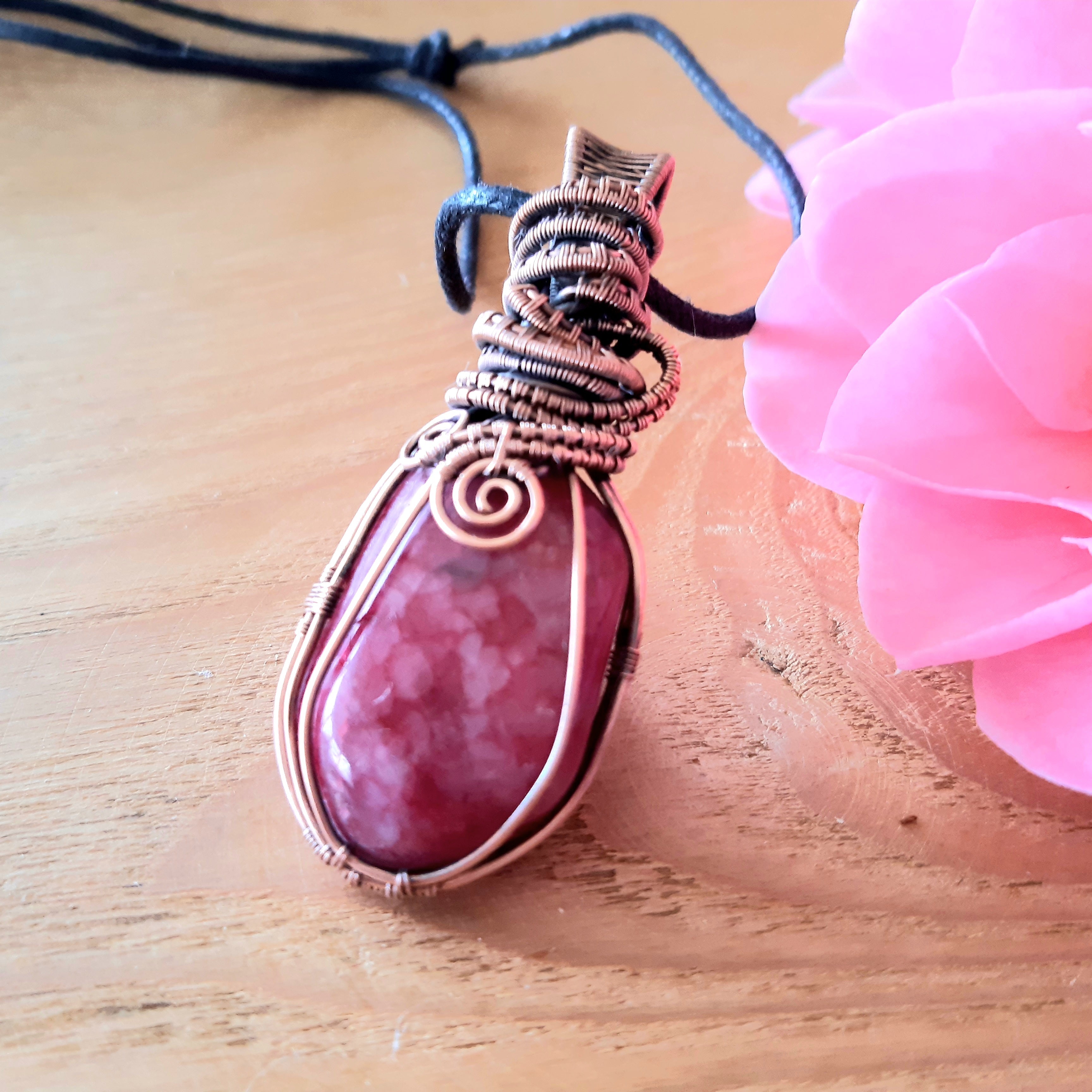 Pink pendant with silver wire wrapping on a wooden surface with a pink flower.