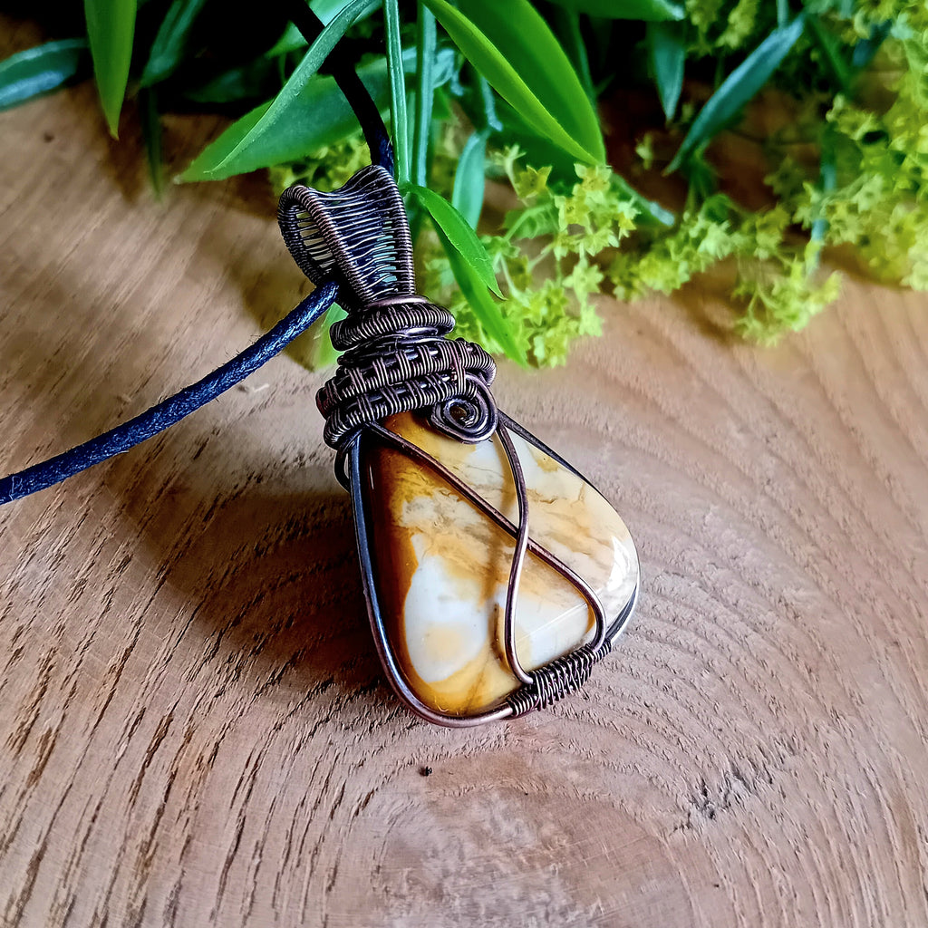 Wire-wrapped stone pendant on a wooden surface with greenery