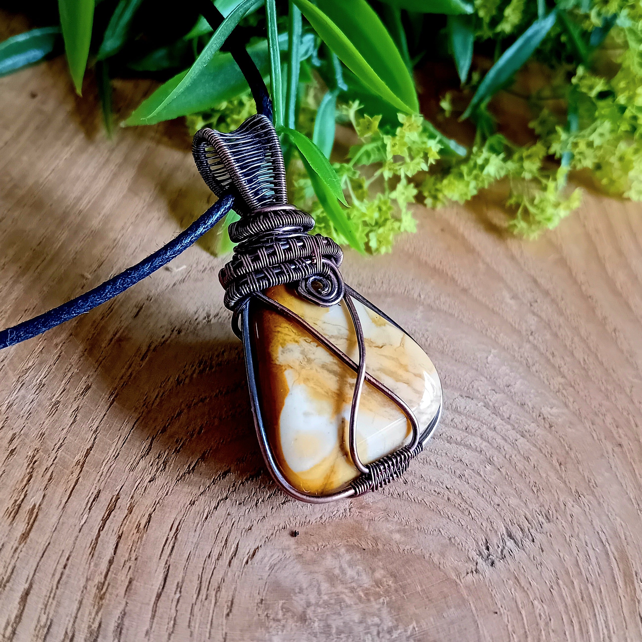 Wire-wrapped stone pendant on a wooden surface with greenery