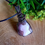Necklace with a pink stone pendant on a wooden surface with greenery in the background