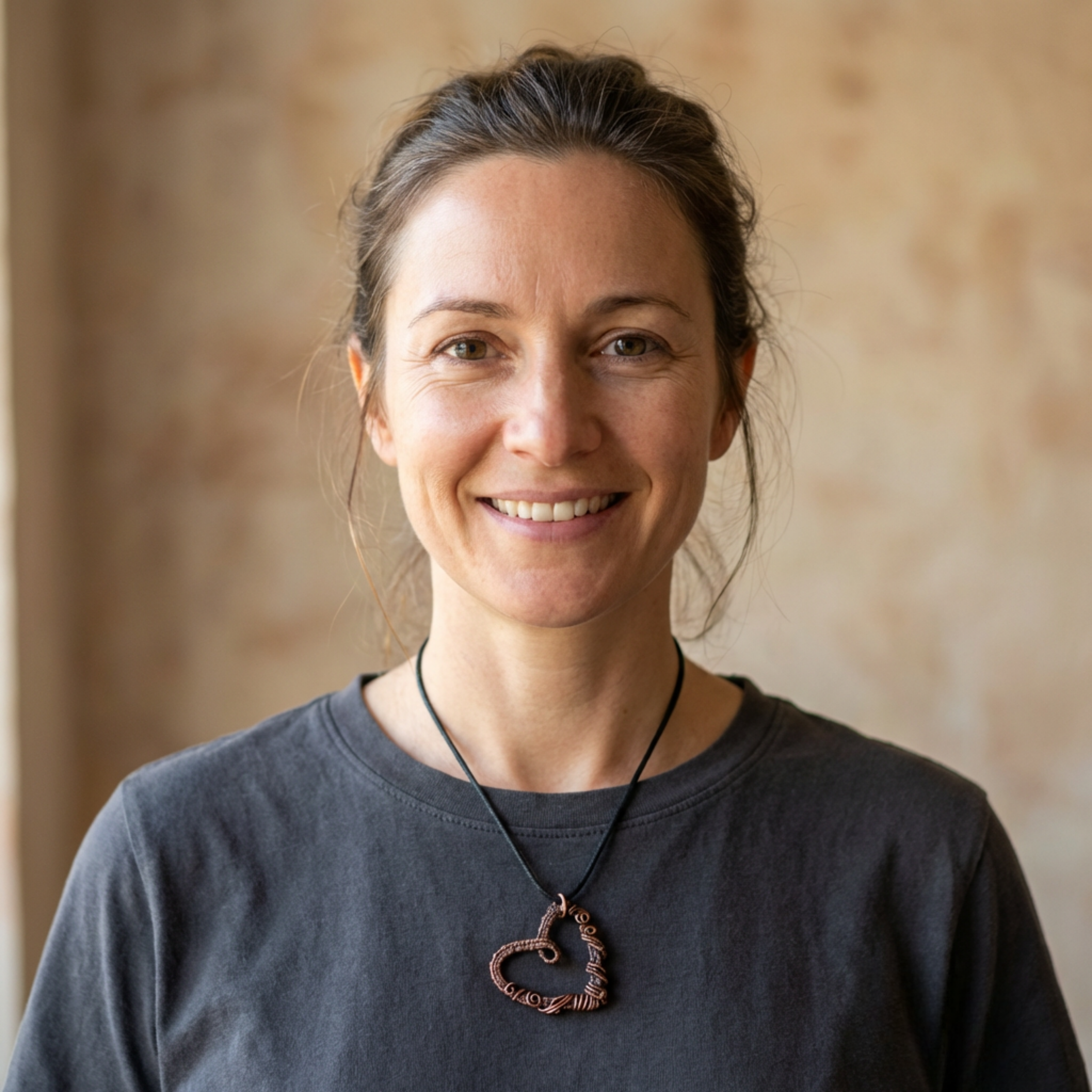 Woman wearing a dark shirt with a heart necklace against a beige wall