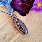 Copper pendant on a wooden surface with flowers in the background