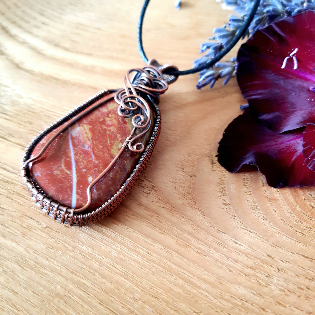 Jasper pendant necklace on a wooden surface with a purple flower