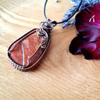 Jasper pendant necklace on a wooden surface with a purple flower