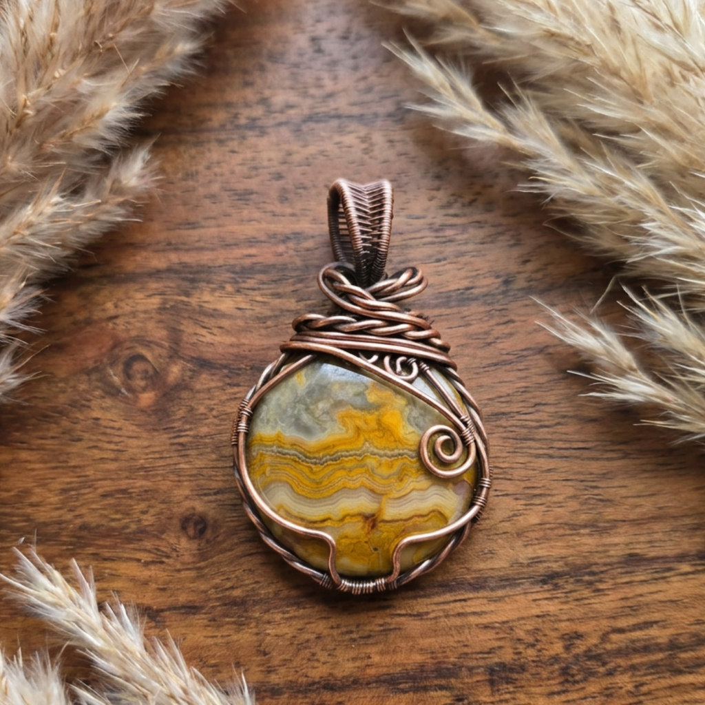 Copper-wrapped pendant with a stone on a wooden surface with dried grasses.