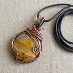 Necklace with a stone pendant wrapped in copper wire on a beige fabric background