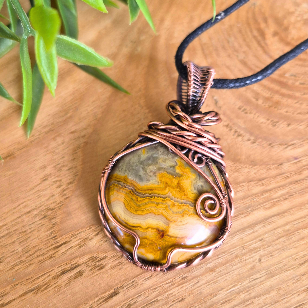 Copper-wrapped stone pendant on a wooden surface with a plant in the background