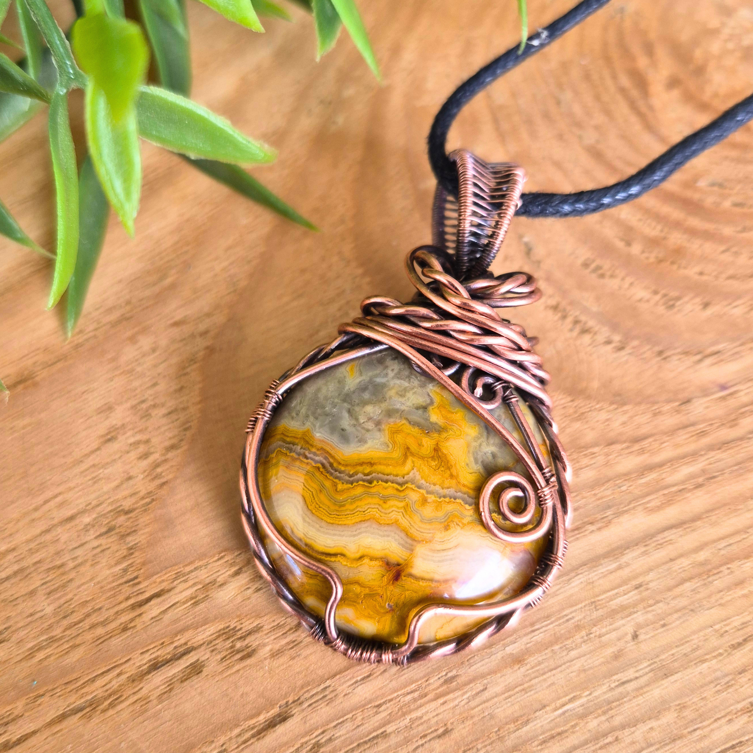Copper-wrapped stone pendant on a wooden surface with a plant in the background