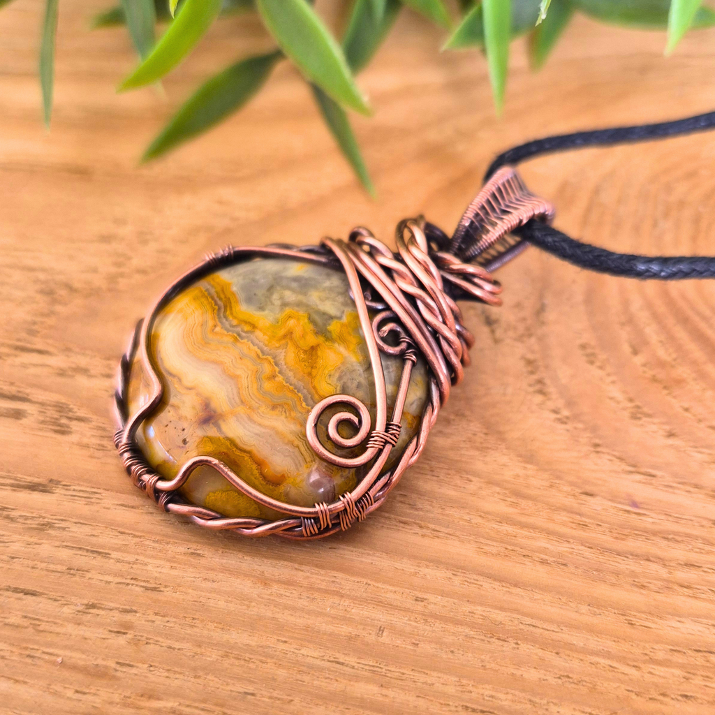 Pendant necklace with a stone and copper wire wrapping on a wooden surface