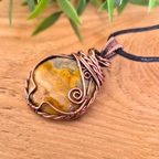 Pendant necklace with a stone and copper wire wrapping on a wooden surface