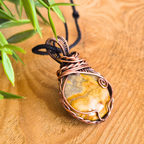 Copper-wrapped pendant with a yellow stone on a wooden surface