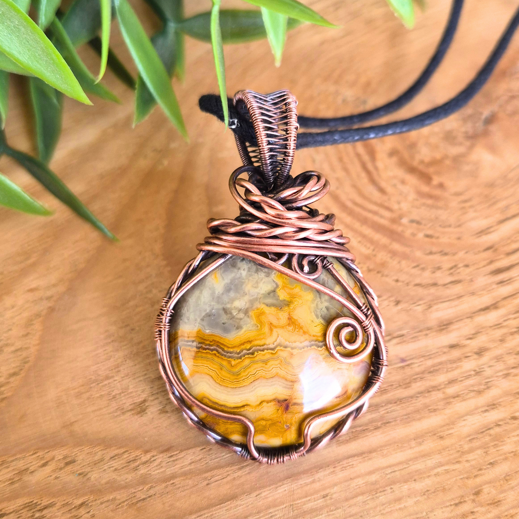 Copper-wrapped pendant with a natural stone on a wooden surface with green leaves in the background
