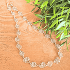 Silver necklace on a wooden surface with green leaves